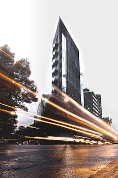Urban cityscape featuring modern high-rise building and dynamic light trails at night.