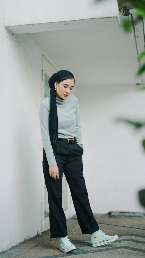 A Woman in Gray Turtleneck Sweater and Black Pants Standing Near the White Wall