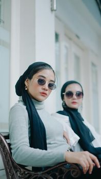 Two fashionable women with sunglasses and elegant attire in an outdoor setting in Indonesia.