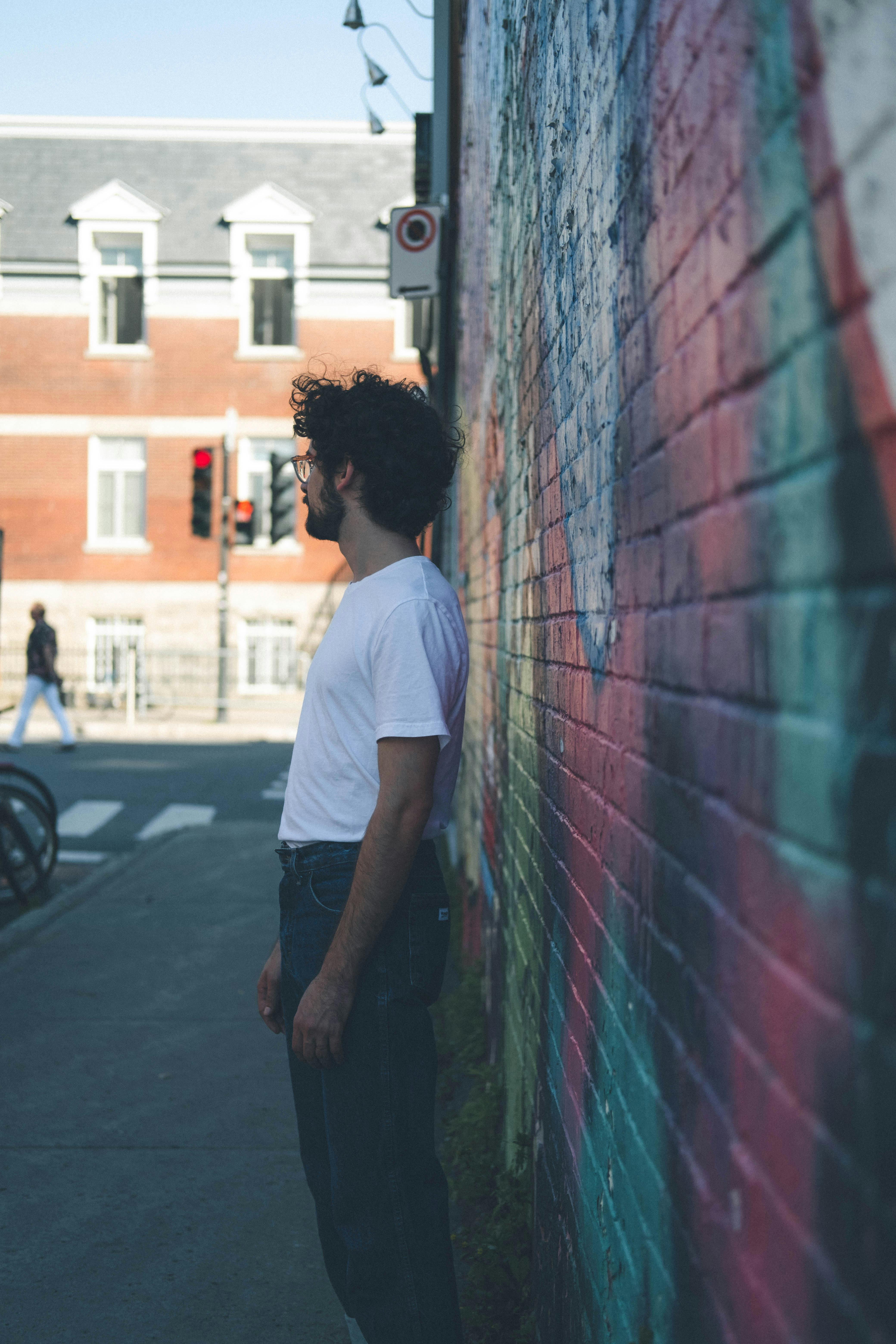 A man in a white shirt stands beside a vibrant graffiti-covered brick wall in an urban setting.