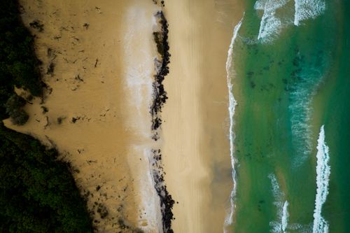 Free Drone shot capturing a stunning aerial view of a secluded beach with clear turquoise waters and lush greenery. Stock Photo