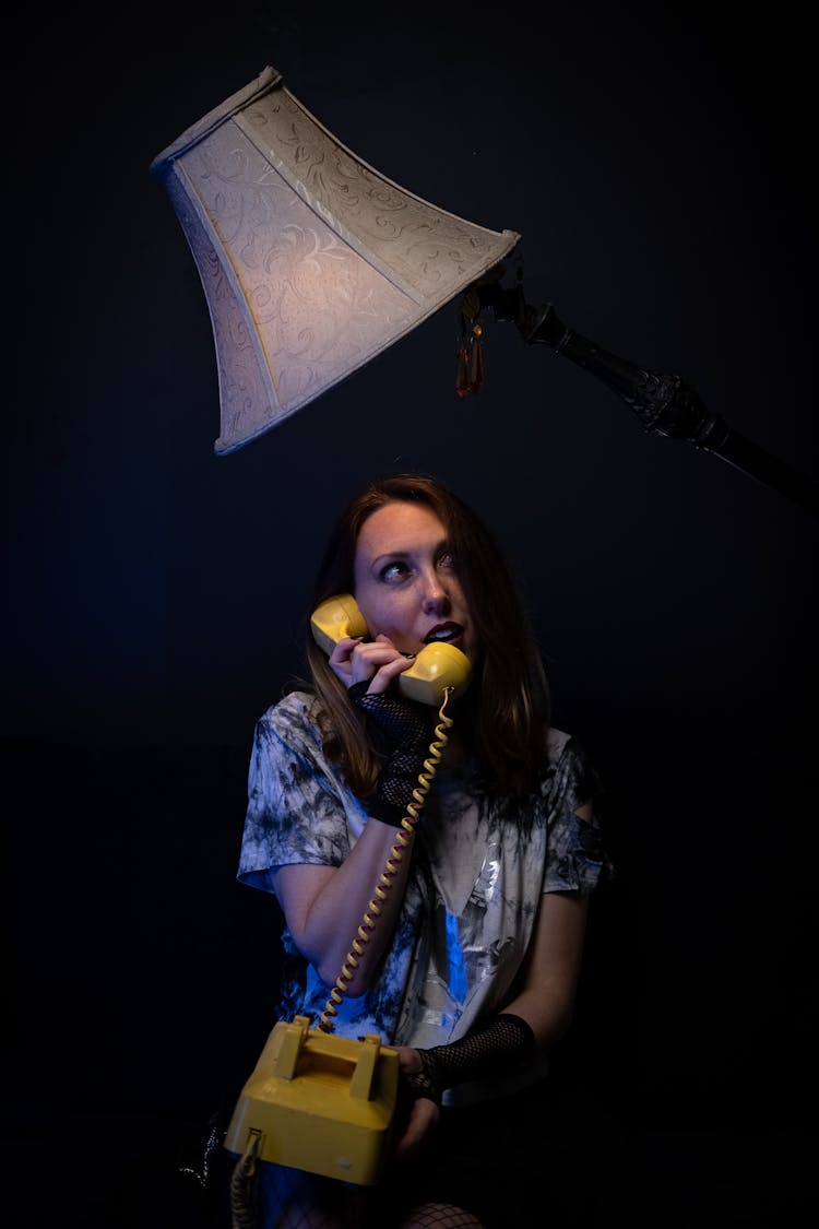 Woman Standing In Printed Shirt Talking On Yellow Vintage Telephone