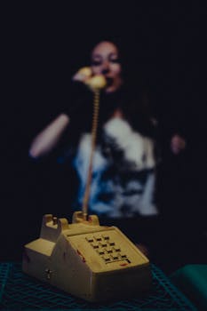 A retro landline phone captured with a woman talking in the background. Vintage feel.