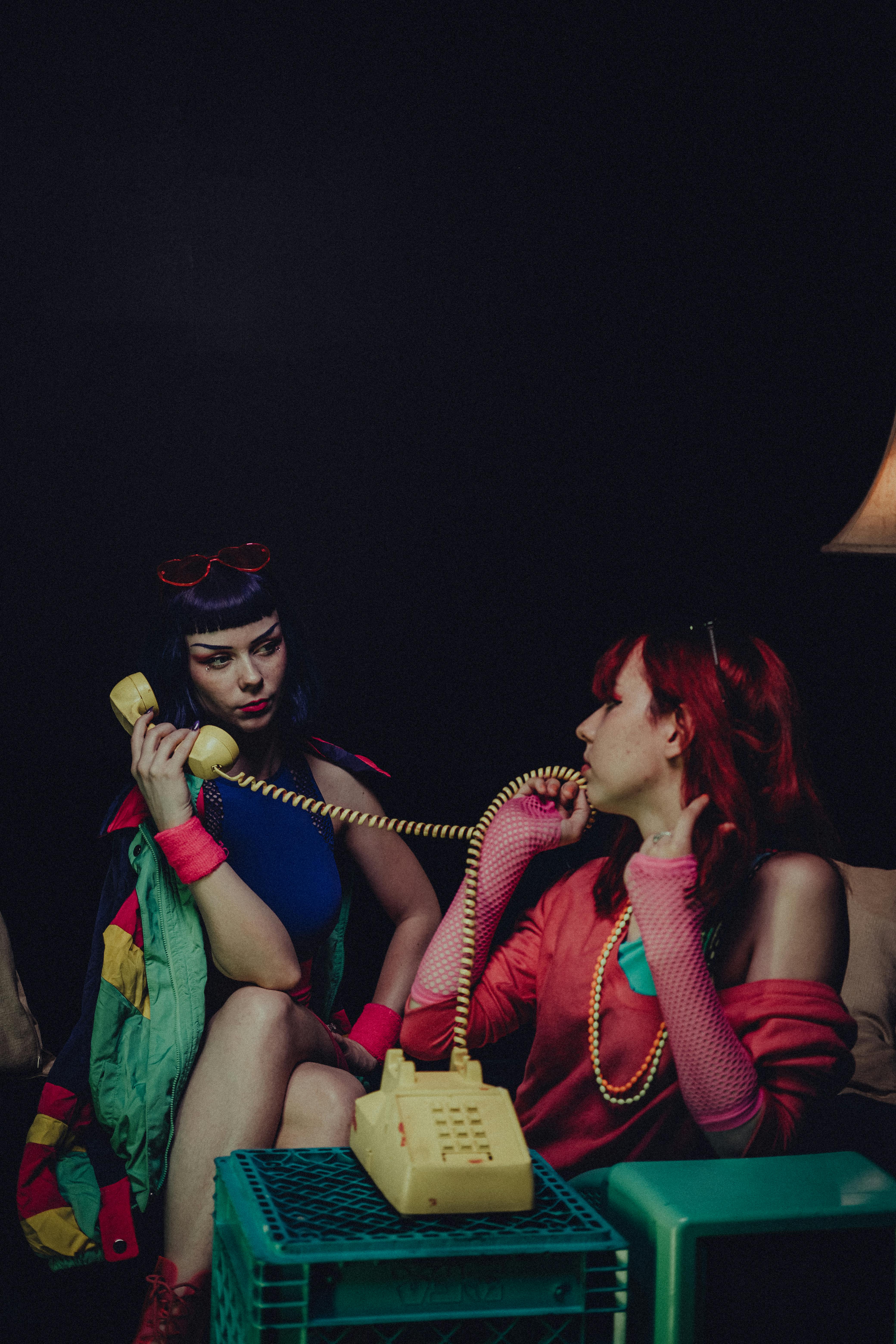 Two women embrace 80s retro fashion while using vintage telephones, creating a nostalgic scene.