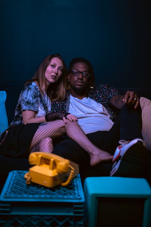 Free Stylish couple posing in a studio with a yellow retro phone, highlighting a fashion-forward and dramatic atmosphere. Stock Photo