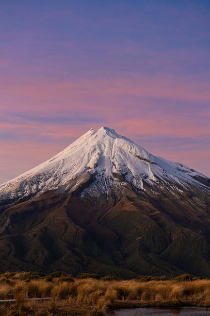 A breathtaking view of snow-capped Mount Taranaki during sunset with a scenic sky.
