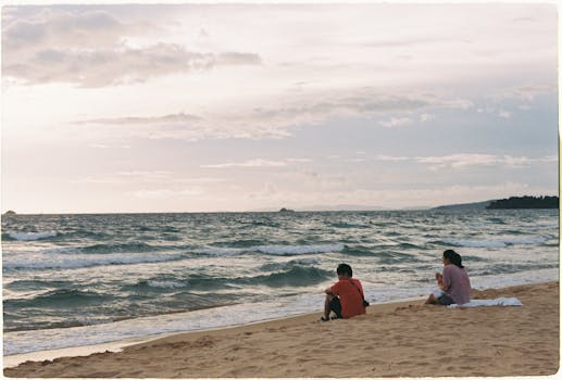 Two people sitting on a sandy beach, enjoying the ocean view at sunset.