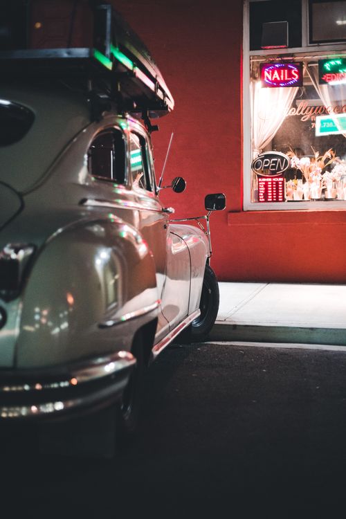 Free Classic vintage car parked by a neon-lit salon at night, showcasing retro vibes. Stock Photo