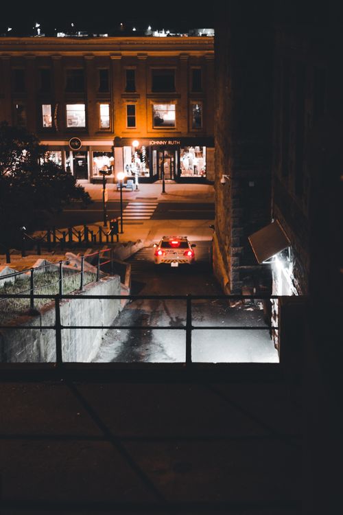 Free A car drives through an urban street lit by building lights and street lamps at night. Stock Photo