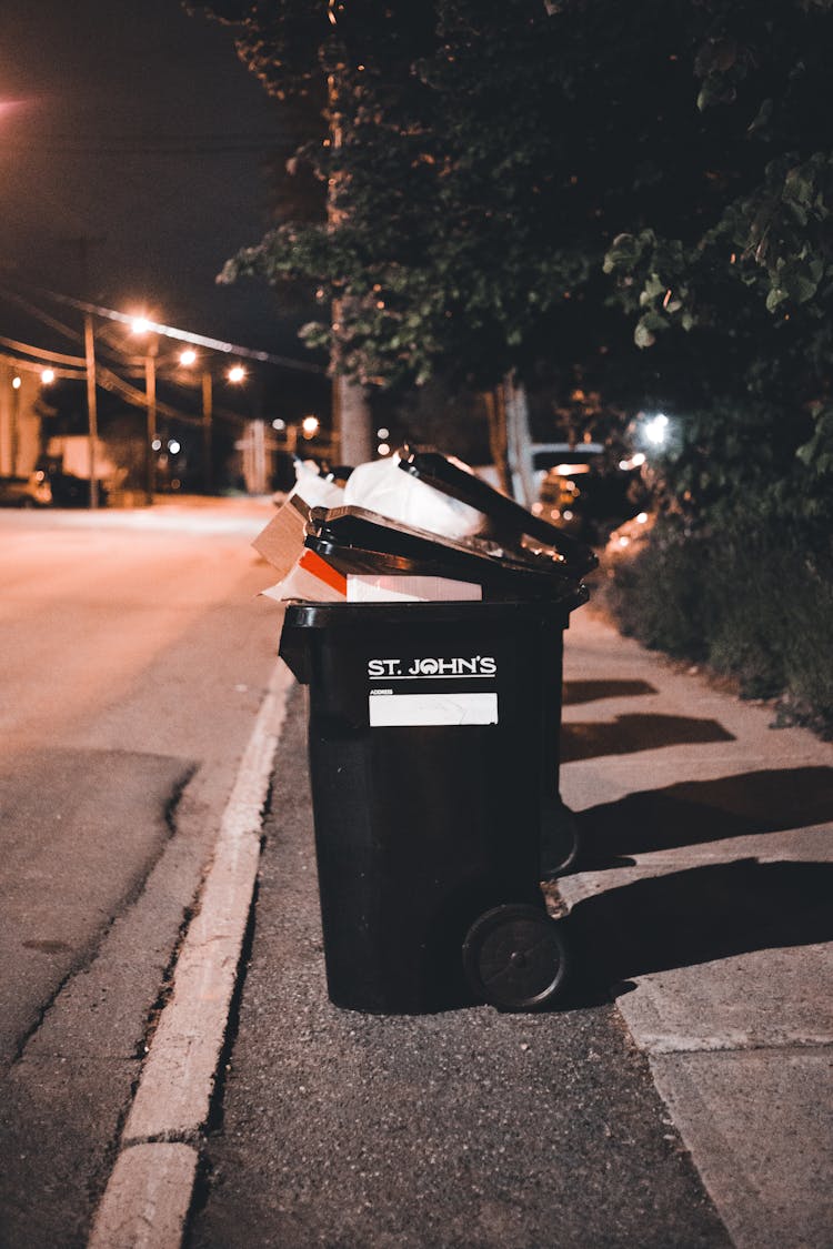 Full Garbage Bins Standing Along A Sidewalk At Night