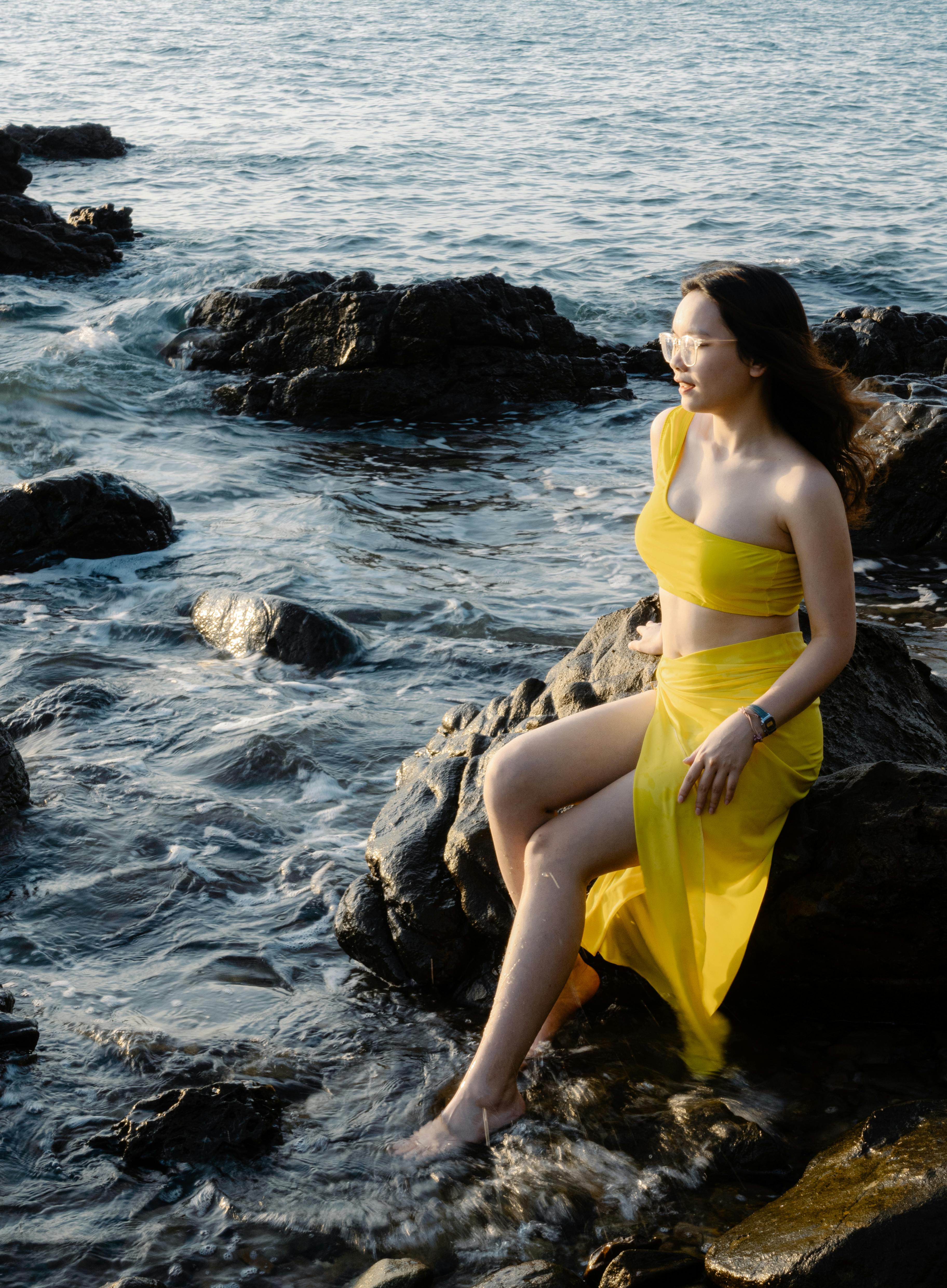 Free A woman in a yellow swimsuit poses on rocks by a beach in Quảng Ninh, Vietnam during the day. Stock Photo
