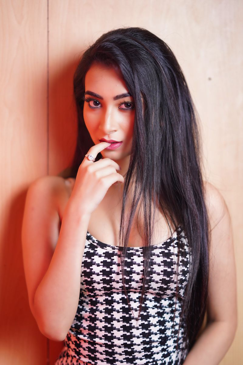 A striking portrait of a woman with long black hair, posing indoors with finger on lips.