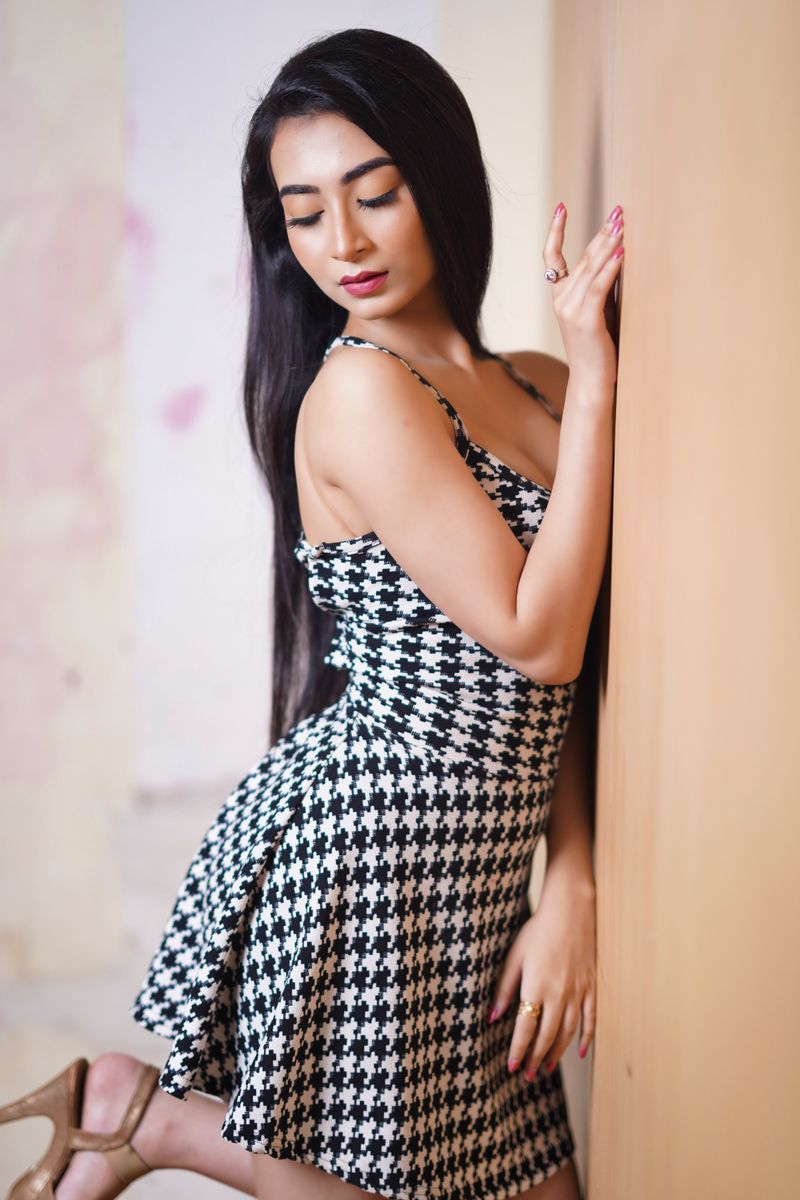 A young woman in a houndstooth dress poses gracefully indoors, exuding elegance and style.