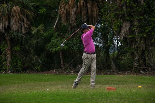 Free Adult male golfer swinging a club on a lush, green golf course surrounded by trees. Stock Photo