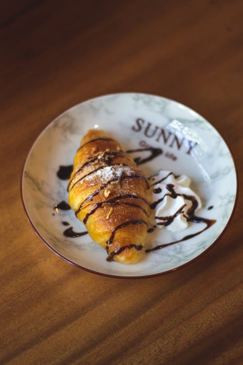 Croissant Drizzled with Chocolate Syrup with Whipped Cream on Side