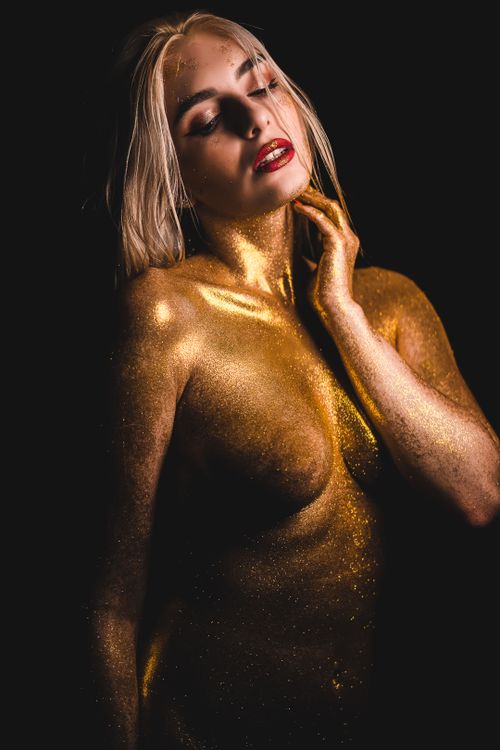 Free Artistic portrait of a woman covered in golden glitter on a dark background. Stock Photo