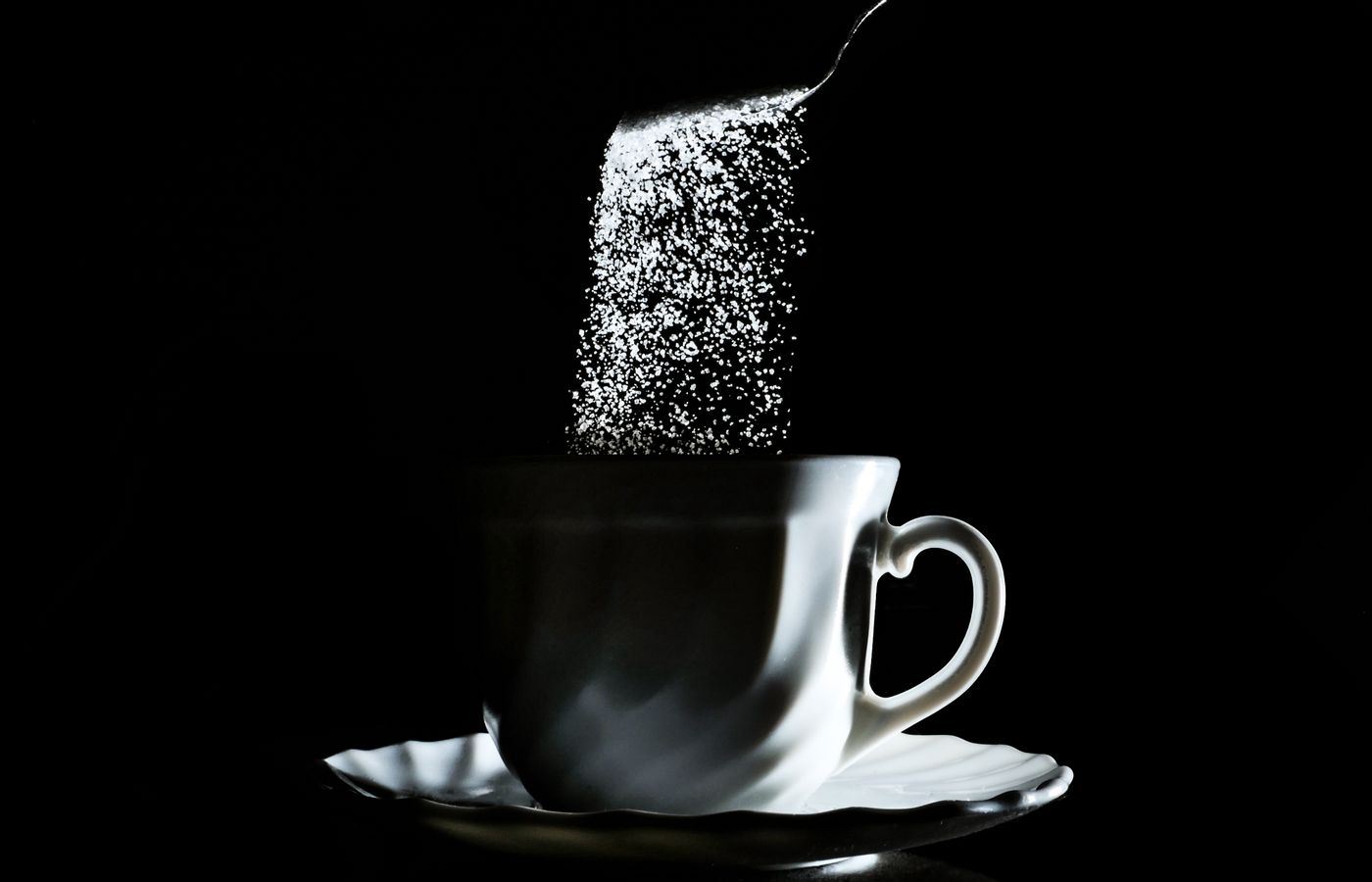 Black and white photo of sugar falling into a coffee cup, creating a dramatic still life scene.
