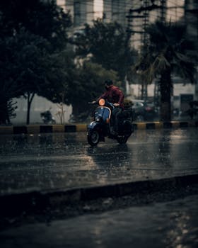 A motorcyclist wearing a red jacket rides through the rain on a wet street in Islamabad, Pakistan.