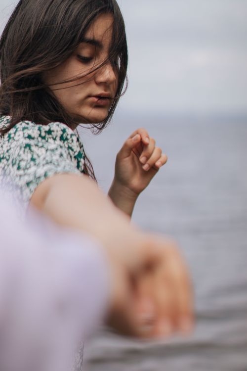 Free A young woman reaches out towards the camera with an introspective expression by the sea. Stock Photo