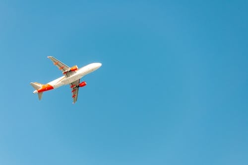 White and Orange Airplane Flying in the Blue Sky