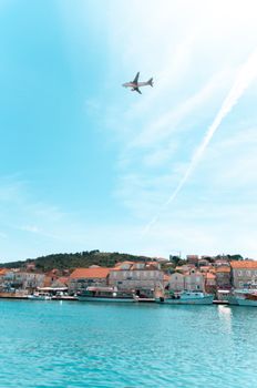 Airplane flying over Trogir waterfront with blue skies, a scenic view in Croatia.