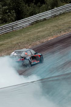 A sports car drifts on a track, creating smoke from its tires in an outdoor setting.