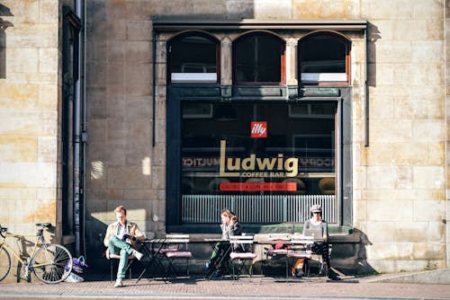 Three People Sitting on Bench in Front of Ludwig Coffee Bar