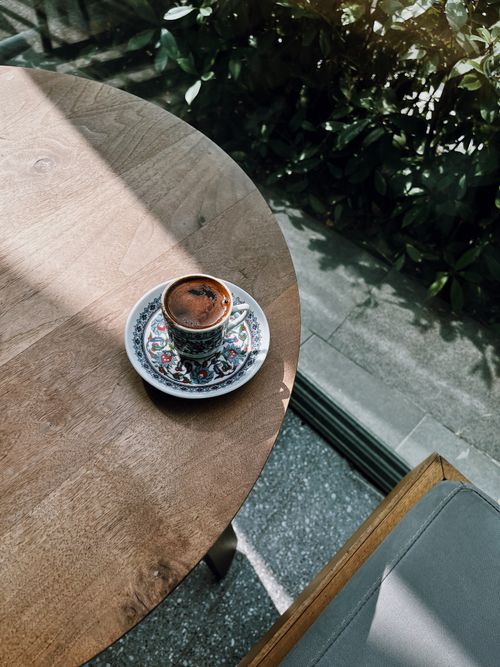 Free A beautifully detailed coffee cup with ornate designs sitting on a wooden table outdoors, perfect for a coffee break. Stock Photo