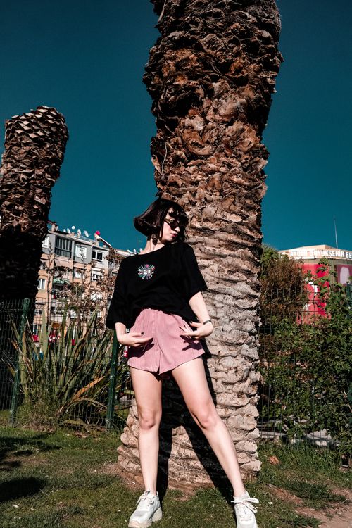 Free A fashionable woman in streetwear poses confidently by palm trees in an urban setting. Stock Photo