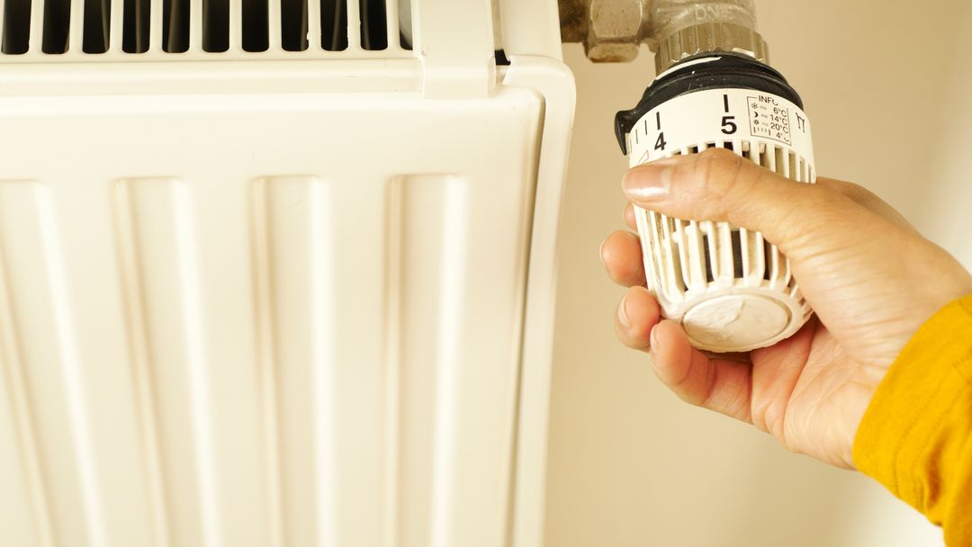 A hand adjusting a valve on a heating pipe