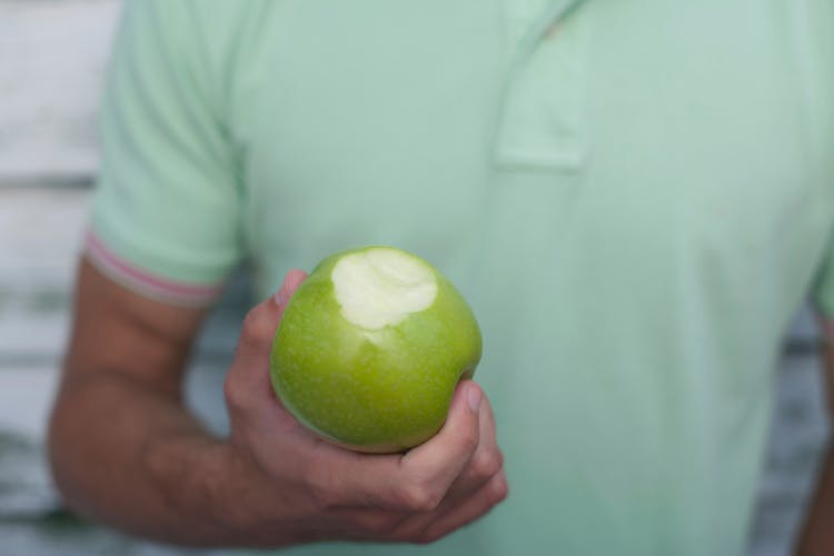 Close-up Photo Of A Person Holding Green Apple With Bite