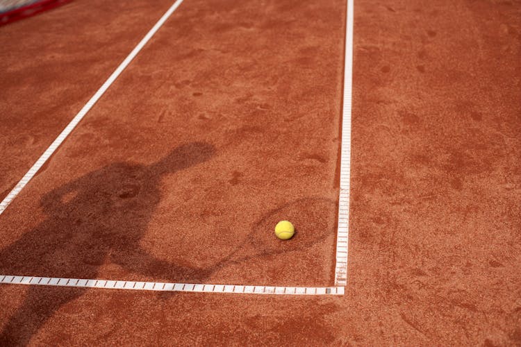 Tennis Player Casting A Shadow On A Tennis Ball Lying On The Court