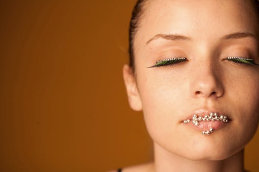 Close-up portrait of a woman with artistic eye makeup and beads on lips, eyes closed.