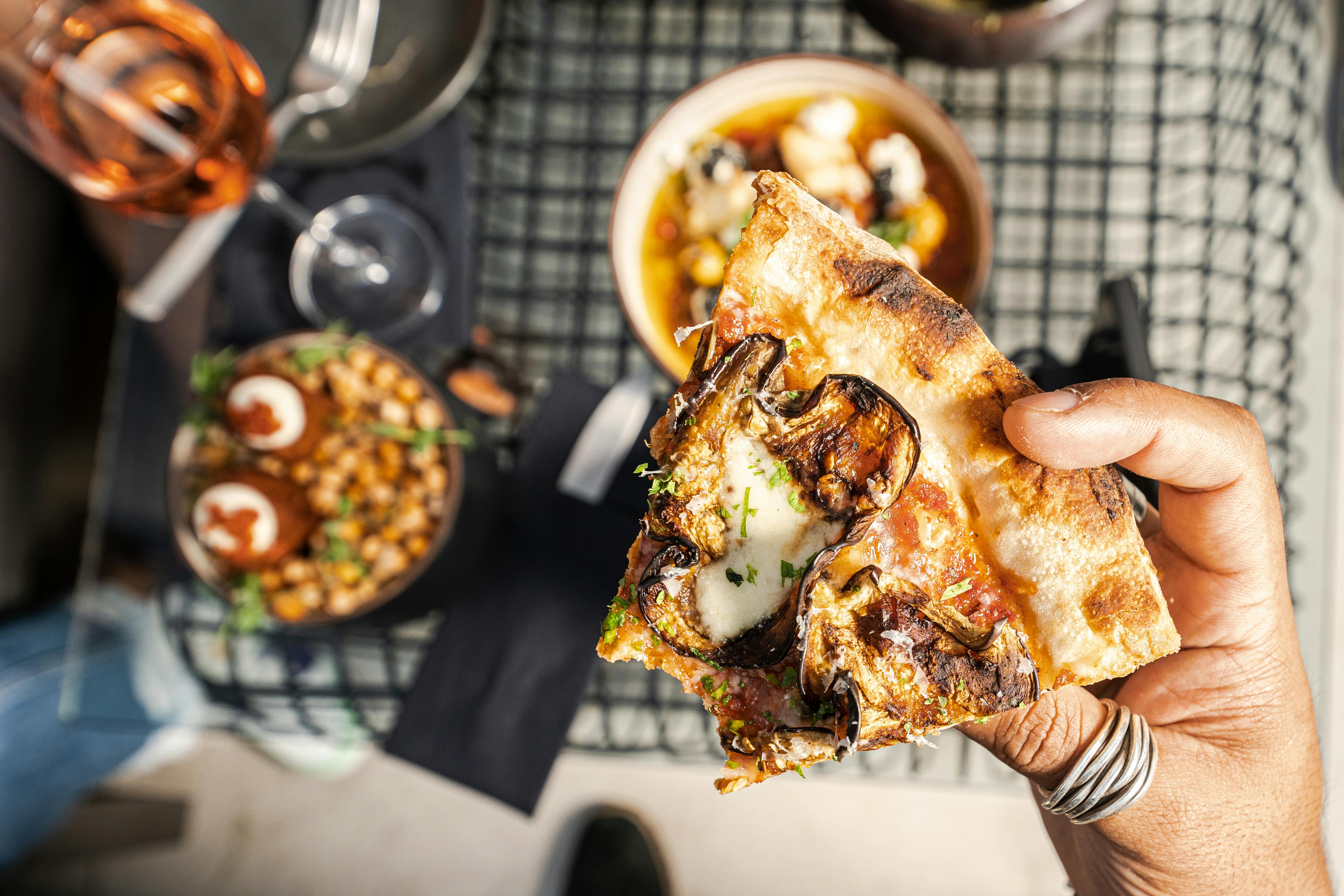 Close-up of a hand holding a tasty pizza slice with mushroom topping in a dining setting.
