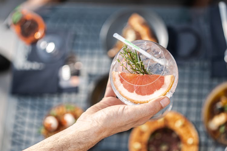 Man Holding A Cocktail Glass With A Slice Of Red Grapefruit And Thyme Twig