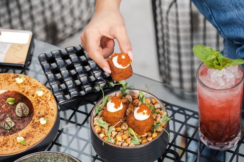 Free Hand picking falafel with caviar from a dish with chickpeas and a refreshing drink nearby. Stock Photo