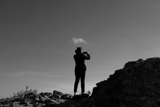 Silhouette of a person capturing the scenery on rocky terrain in black and white.