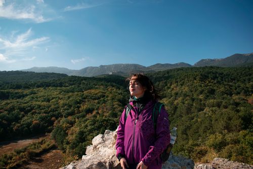 Free Woman enjoying a mountain view while hiking in a purple jacket, surrounded by nature. Stock Photo