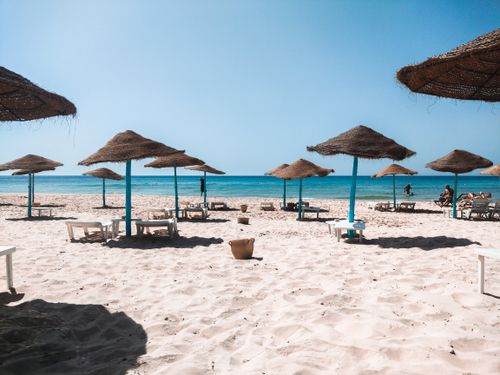 Free Peaceful sandy beach with straw umbrellas and clear blue sea under a bright sky. Stock Photo