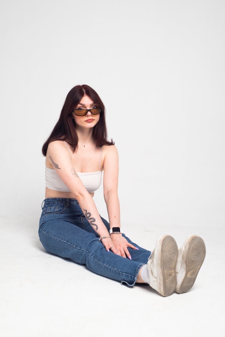 Studio Shot Of Woman In Jeans Sitting With Stretched Legs