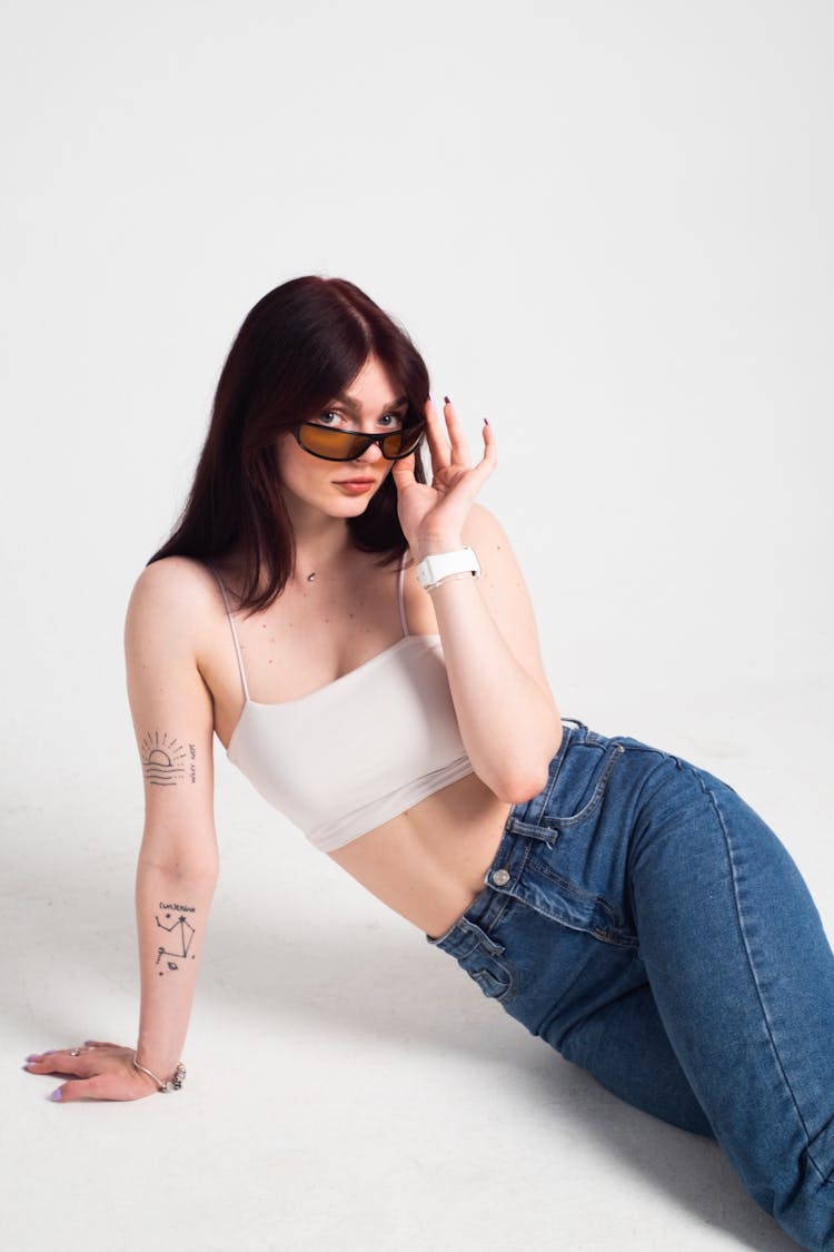 Studio Shot Of Woman With Sunglasses And Jeans Leaning On One Hand 