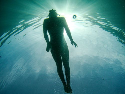 Free Underwater silhouette of a diver swimming toward the surface with sunlight streaming through water. Stock Photo