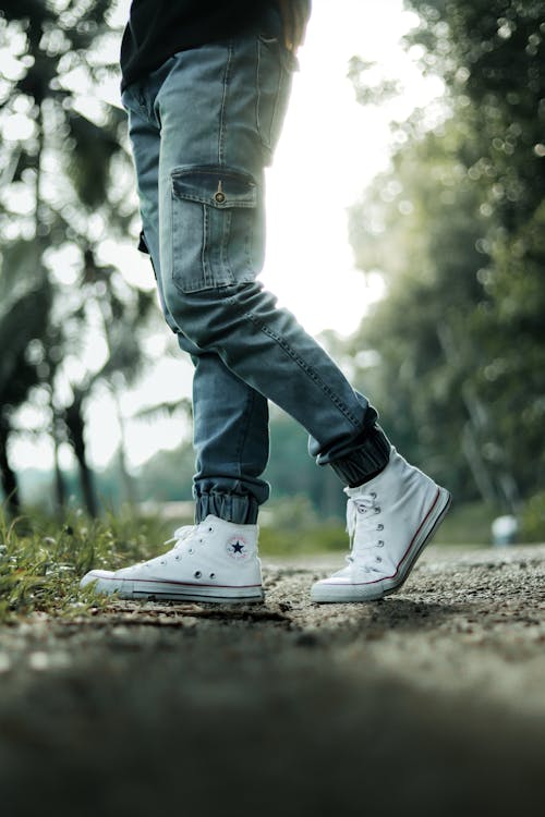 Free Person in Blue Denim Jeans and White Nike Sneakers Standing on Brown Dirt Road Stock Photo