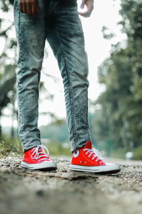 Free Close-up of red sneakers paired with denim on a scenic outdoor path in KL, India. Stock Photo