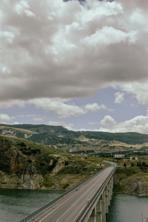 Free Dramatic scenery with a bridge crossing a river amidst rolling countryside and majestic mountains. Stock Photo