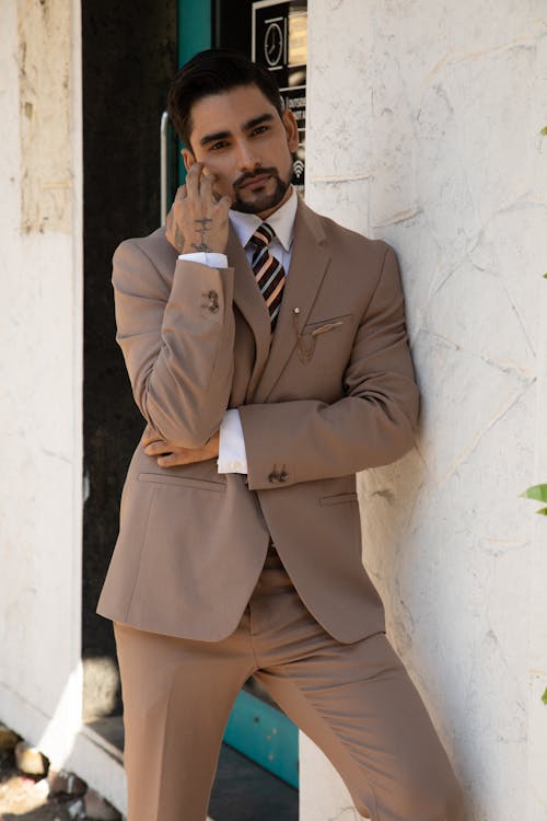 A Man in Brown Suit Leaning on White Wall