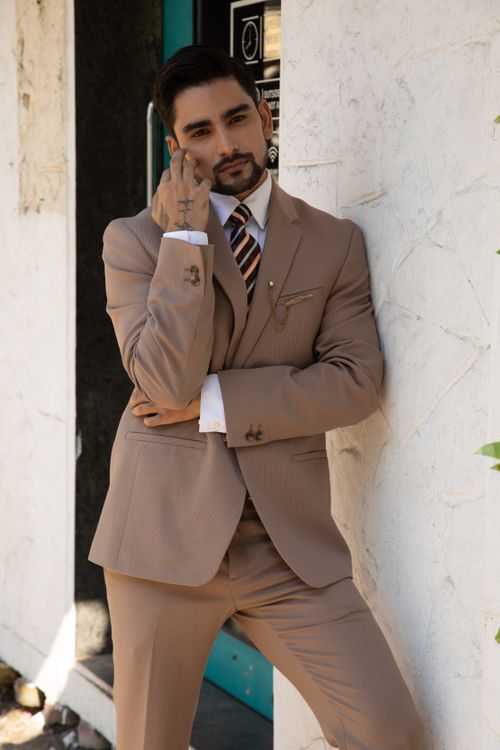 Free Fashionable man in a suit leaning casually against a wall outdoors. Stock Photo