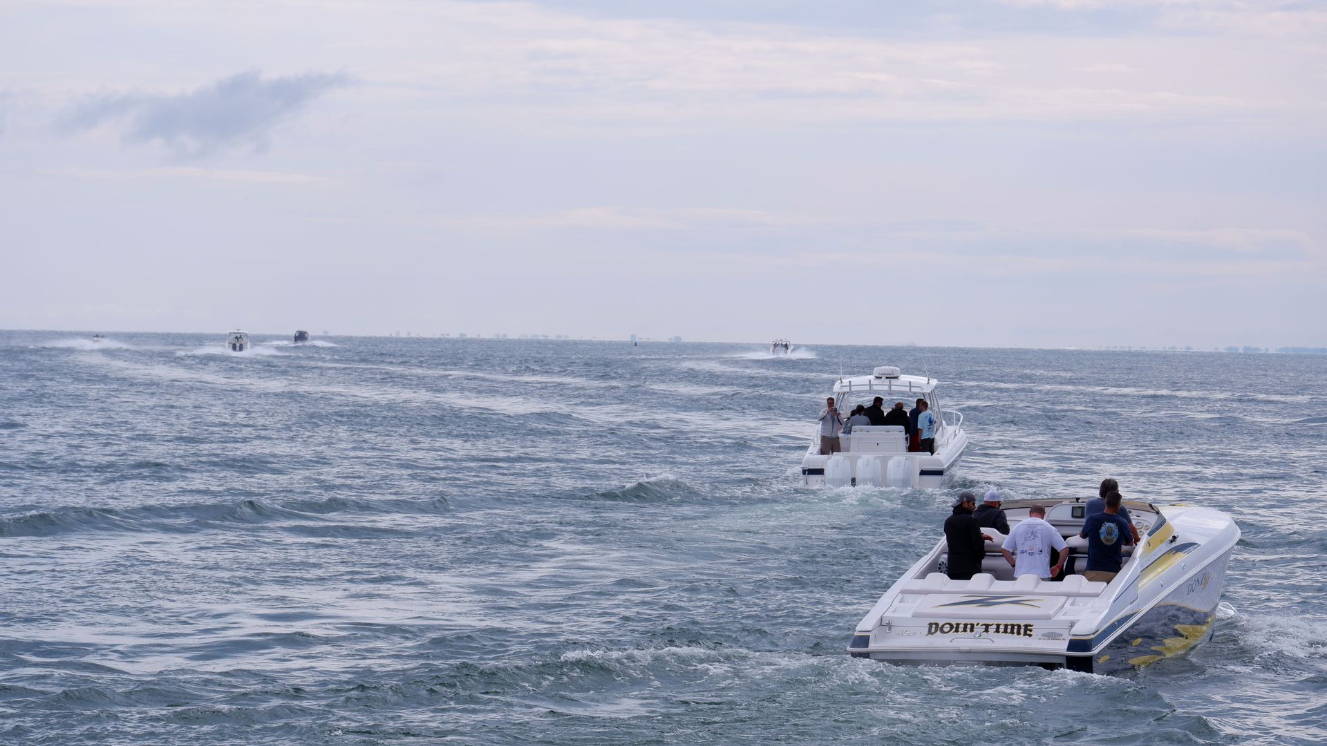 A group of speedboats cruising on open sea waters under a partly cloudy sky.