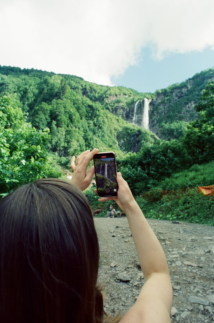 Woman Taking A Video Of A Waterfall In The Mountain