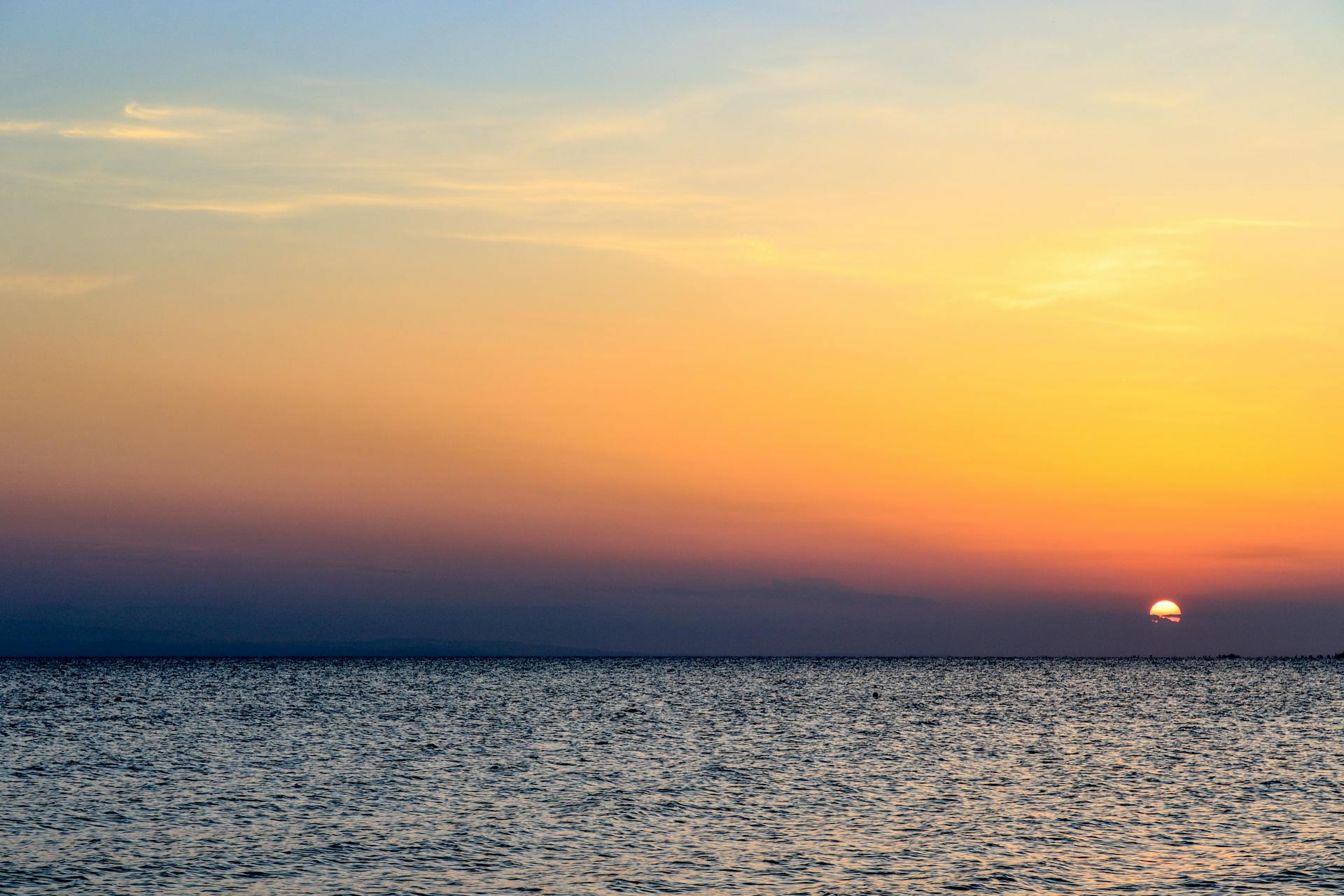 Capture of a vibrant sunset over the Aegean Sea from Nea Irakleia, Greece, showcasing colors of the sky merging with the ocean.